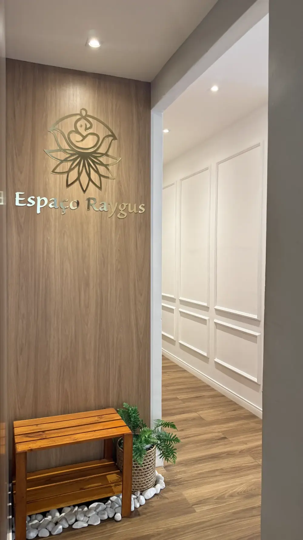 Recepção do Espaço Raygus com logotipo dourado em parede de madeira e banco