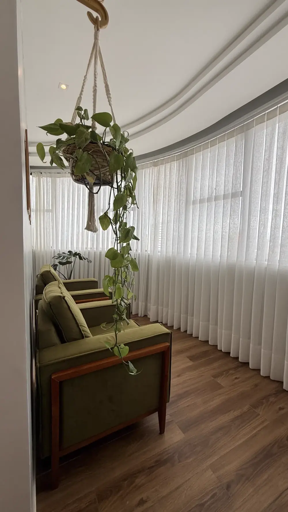 Sala de espera com poltronas verdes e plantas junto às cortinas